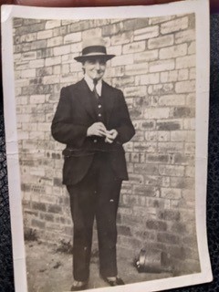 Image of a black and white photograph depicting Martha stood in front of a brick wall. The photograph is dated to circa 1940.  Martha is wearing a three-piece suit, tie and hat. 