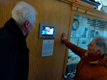 A man and woman watching a film on an iPad mounted on a wall